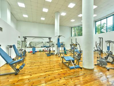 Ruime fitnessruimte met houten vloer, witte zuilen en diverse fitnessapparaten.