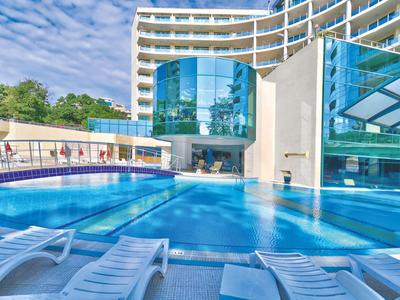 Modern hotelzwembad met ligstoelen en grote glazen gevel bij zonnig weer.