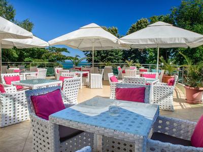 Terras met witte zitmeubels, kleurrijke kussens en parasols met uitzicht op een groen landschap.