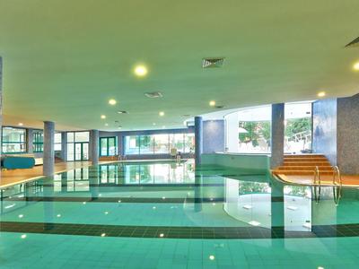 Nowoczesny basen kryty z dużymi oknami i drewnianymi ławkami w spokojnej atmosferze.