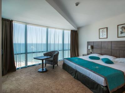 Nowoczesny pokój hotelowy z dużym łóżkiem, miejscem do siedzenia i widokiem na morze przez okna od podłogi do sufitu