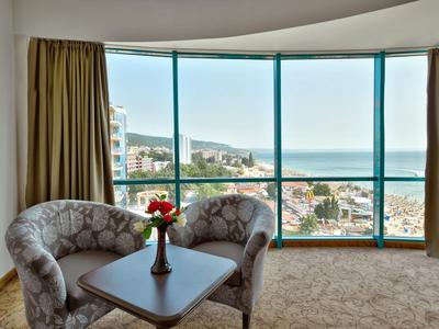 Pokój hotelowy z dwoma fotelami, stołem i dużymi oknami z widokiem na morze.