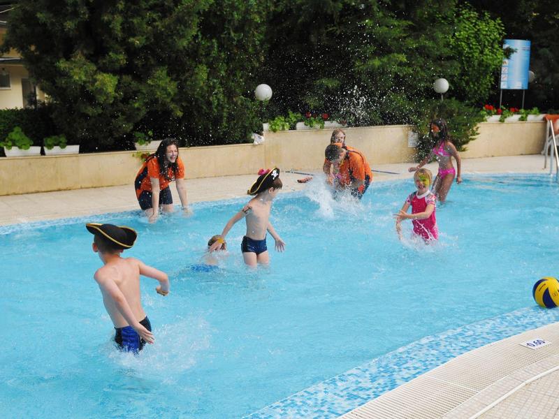 Dzieci bawiące się i skaczące w zewnętrznym basenie hotelowym przy ładnej pogodzie.