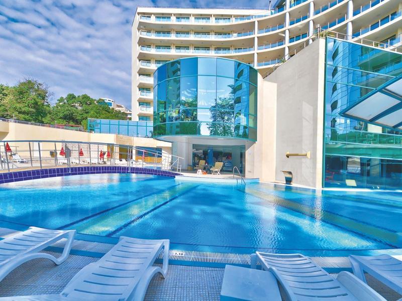 Nowoczesny basen hotelowy z leżakami i szklaną fasadą pod niebieskim niebem