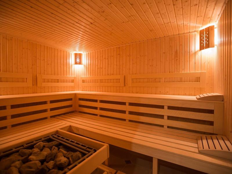 Drewniana sauna z podgrzewanymi kamieniami i wielopoziomowymi siedziskami przy ciepłym świetle.