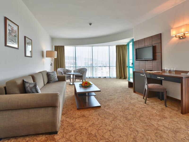 Nowoczesny pokój hotelowy z sofą, telewizorem, biurkiem i dużymi oknami.