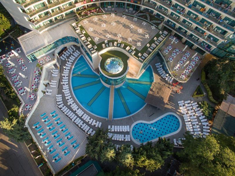 Widok z lotu ptaka na duży basen hotelowy z leżakami i otaczającym kompleksem hotelowym.