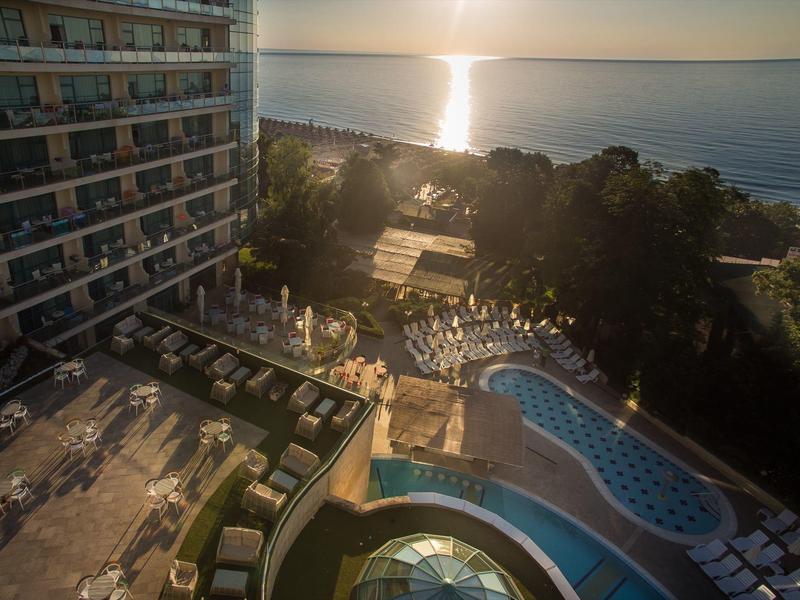 Hotel z basenem i leżakami nad morzem o zachodzie słońca.