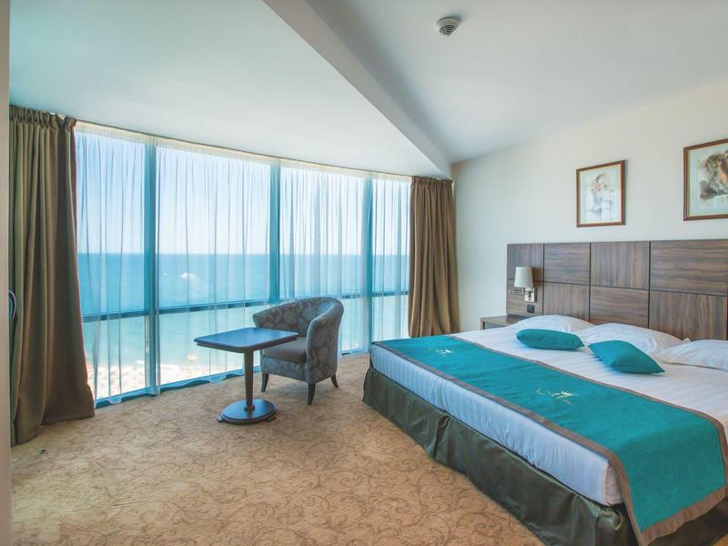 Pokój hotelowy z dużym łóżkiem, widokiem na morze i miejscem do siedzenia z krzesłem i stołem