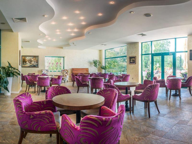 Nowoczesna jadalnia hotelowa z różowymi krzesłami i okrągłymi stołami przy dużych oknach.