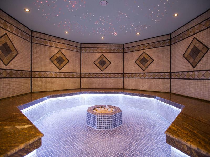 Jasno oświetlony, okrągły basen spa w mozaikowym pomieszczeniu z gwiaździstym sufitem.