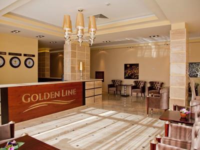 Heller Hotel-Empfang mit braun-beiger Rezeption, Kronleuchter und Sitzgruppen aus Stühlen und Tischen.