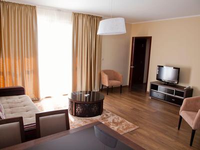 Jasny salon z oknem, brązowymi zasłonami, sofą, fotelami i telewizorem na drewnianej podłodze.