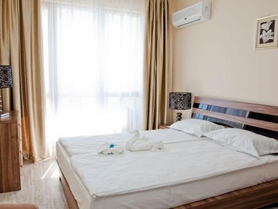 Jasny pokój hotelowy z podwójnym łóżkiem, dwoma stolikami nocnymi i dużymi zasłonami w oknie.