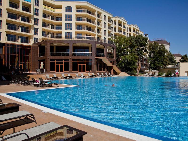 Großer blauer Pool vor mehrstöckigem Hotelgebäude bei sonnigem, klarem Himmel.