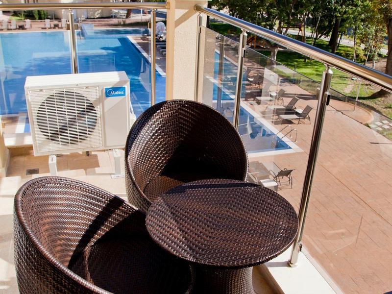 Braune Rattanmöbel mit Tisch auf Balkon, Pool und Bäume im Hintergrund an sonnigem Tag.