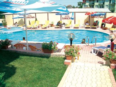 Hotel pool with lounge chairs, umbrellas, and well-maintained garden area.