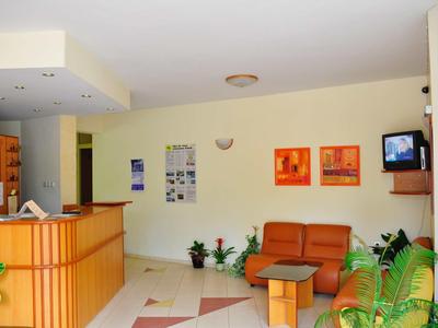 Area di ricevimento dell'hotel luminosa con bancone in legno, divani arancioni e piante.