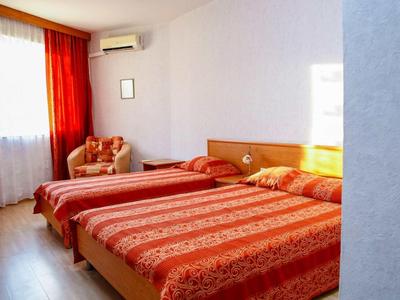 Camera d'hotel con due letti, biancheria rossa a motivi e poltrona imbottita vicino alla finestra.