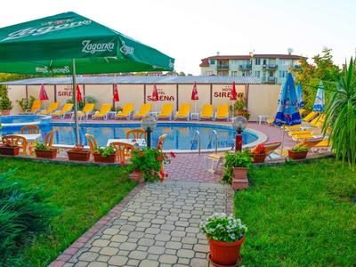 Area piscina dell'hotel con ombrelloni e lettini circondata da vegetazione e sentiero lastricato.