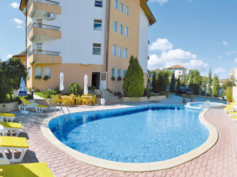 Piscina all'aperto con lettini e ombrelloni davanti a un edificio alberghiero su più piani.