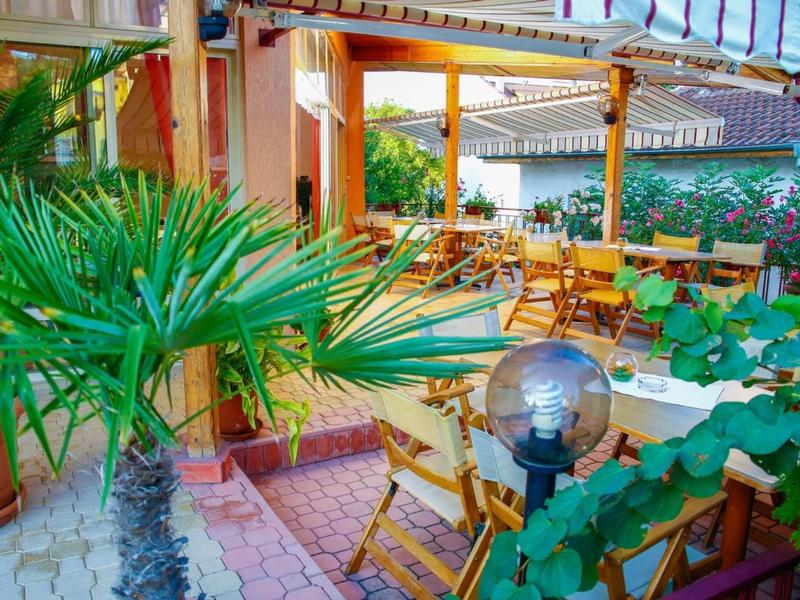 Accogliente terrazza esterna con sedie in legno, tavoli e piante tropicali accanto a un hotel.