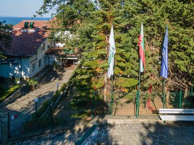 Stinná zahradní oblast s třemi vlajkami a bílou lavičkou vedle domu.