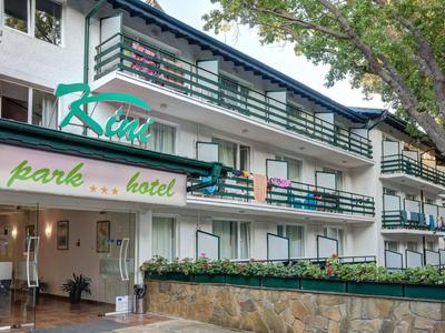 Vícepodlažní hotelová budova s balkony a zeleným označením, obklopená stromy.