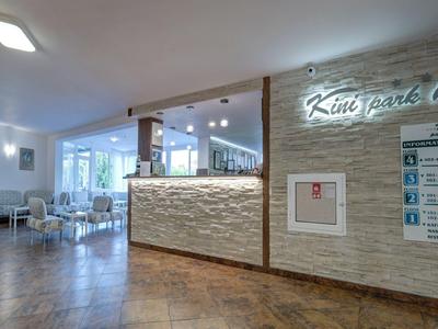 Moderní recepce hotelové restaurace se světlými stěnami a velkými okny.