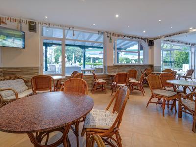 Jasna jadalnia z stolikami i wiklinowymi krzesłami oraz dużymi oknami z widokiem na taras.