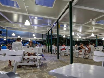 Otevřená jídelna s bílým dřevěným nábytkem a několika lidmi za večerního osvětlení.