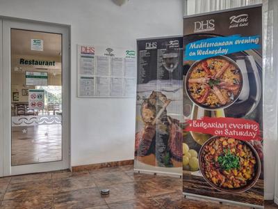 Vchodové dveře do restaurace s reklamními bannerami na středomořská a maďarská jídla uvnitř.