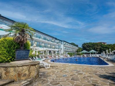 Moderner Hotelpool mit blauen Liegestühlen und Sonnenschirmen, umgeben von grüner Bepflanzung.