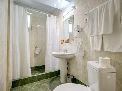 Malá koupelna s toaletou, umyvadlem, sprchovým závěsem a ručníky na stěně.