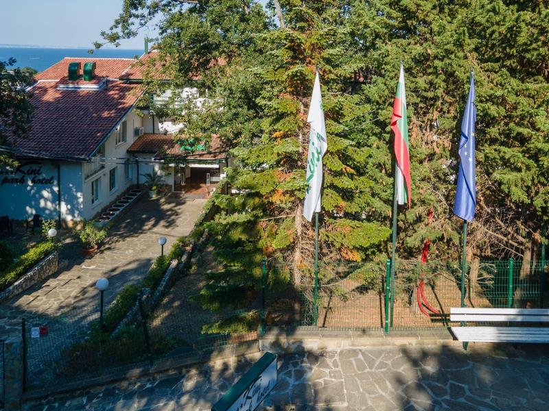 Stinná zahradní oblast s třemi vlajkami a bílou lavičkou vedle domu.