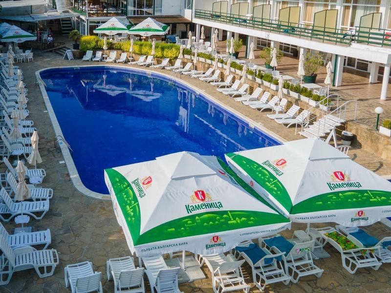 Hotelový bazén s modrým lemem, lehátky a slunečníky na terase.