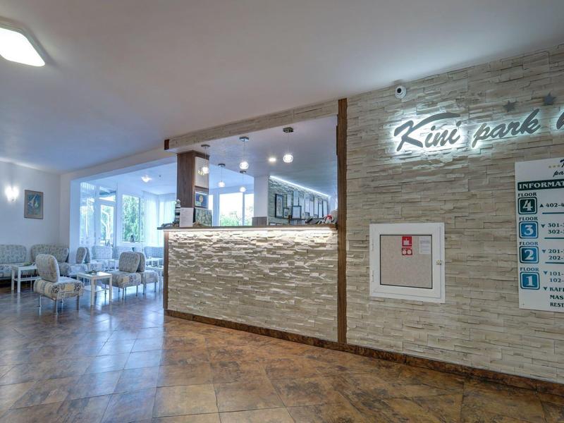 Moderní recepce hotelové restaurace se světlými stěnami a velkými okny.