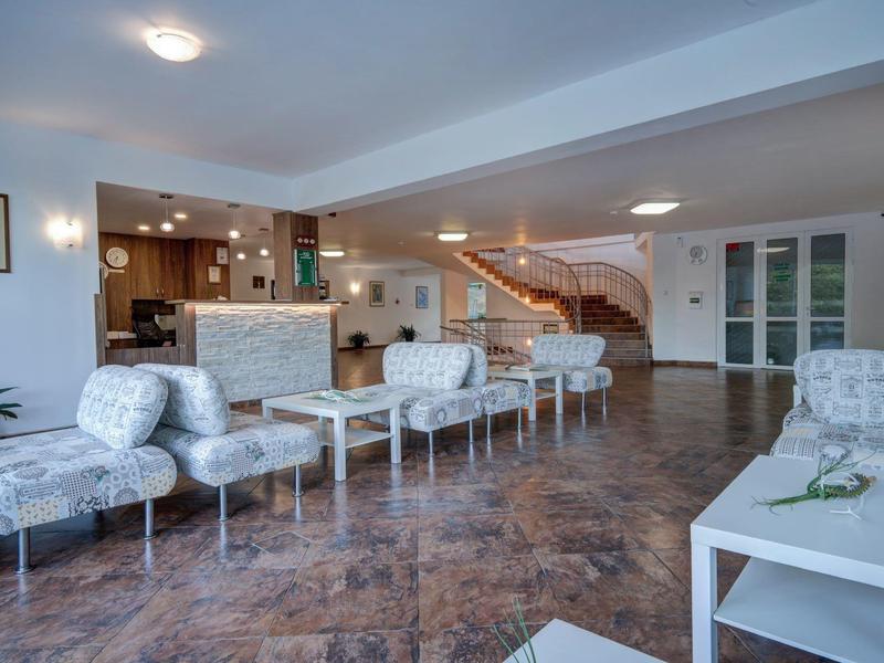 Světlý hotelový salónek s bílými křesly, stoly a schodištěm v pozadí.