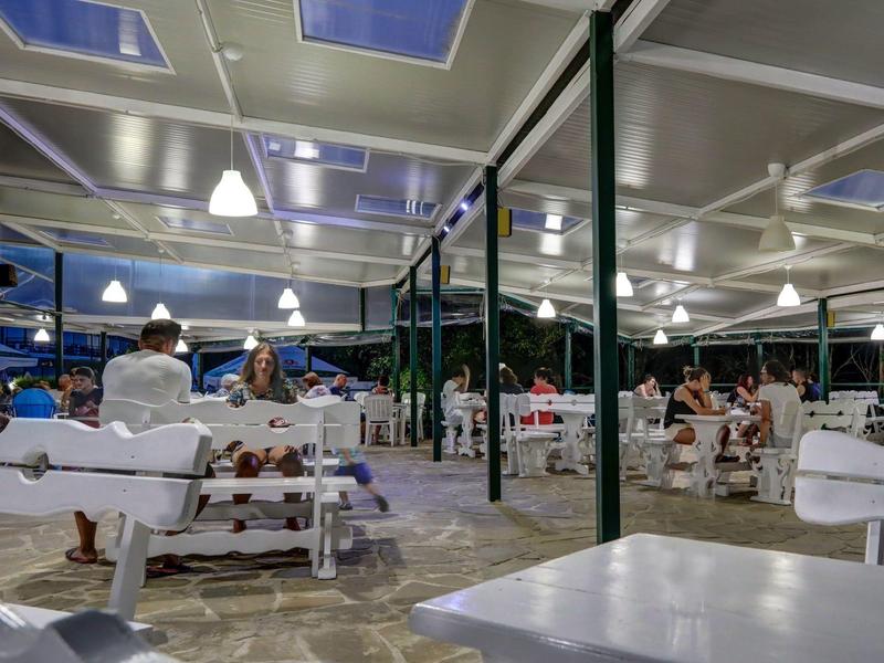 Otevřená jídelna s bílým dřevěným nábytkem a několika lidmi za večerního osvětlení.