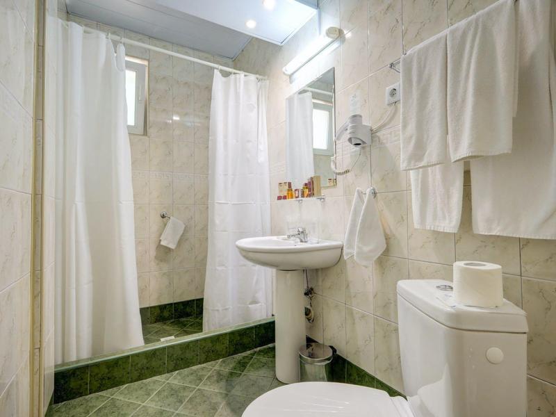 Malá koupelna s toaletou, umyvadlem, sprchovým závěsem a ručníky na stěně.