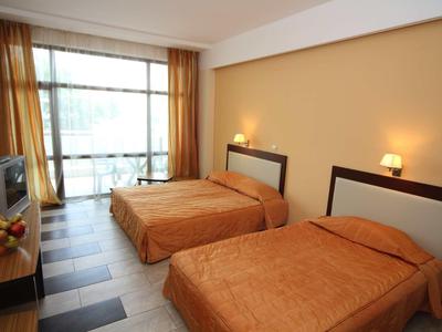 Hotelový pokoj se dvěma postelemi, hnědými závěsy a televizí na stole.