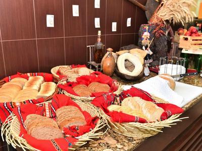 Různorodý snídaňový bufet s chlebem, pečivem a tradiční výzdobou na dřevěném stole.