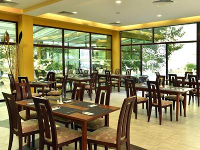 Světla restaurace s mnoha dřevěnými stoly a židlemi, velká okna a výhled na terasu.