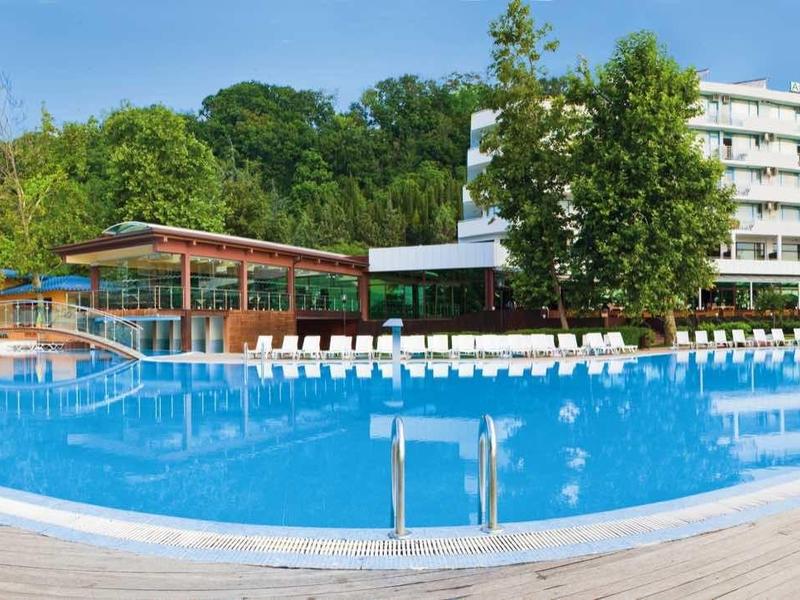 Velká oblast bazénu s lehátky a vícepodlažní hotelovou budovou v pozadí.