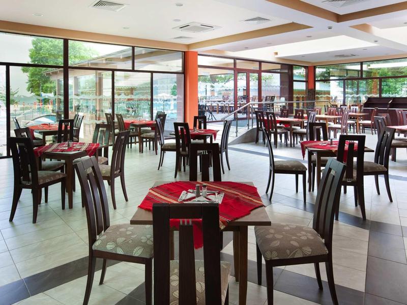 Světlá restaurace s dřevěnými stoly a židlemi, velká okna s výhledem ven.