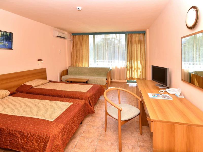 Hotelový pokoj se dvěma postelemi, psacím stolem, židlí, televizí a oknem se závěsy.