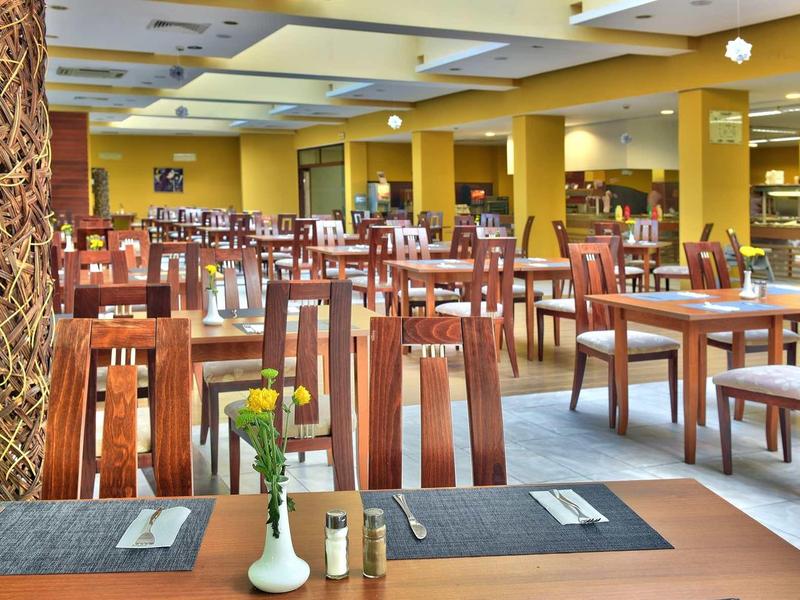 Velká snídaňová místnost s mnoha dřevěnými stoly a židlemi, zdobená světlými a tmavými tóny.