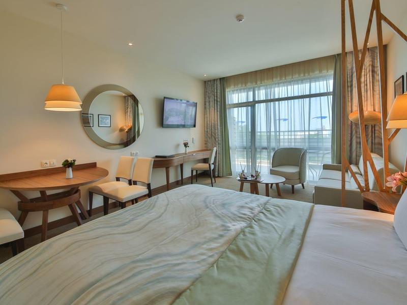 Moderně zařízený hotelový pokoj s postelí, posezením a psacím stolem u velkého okna