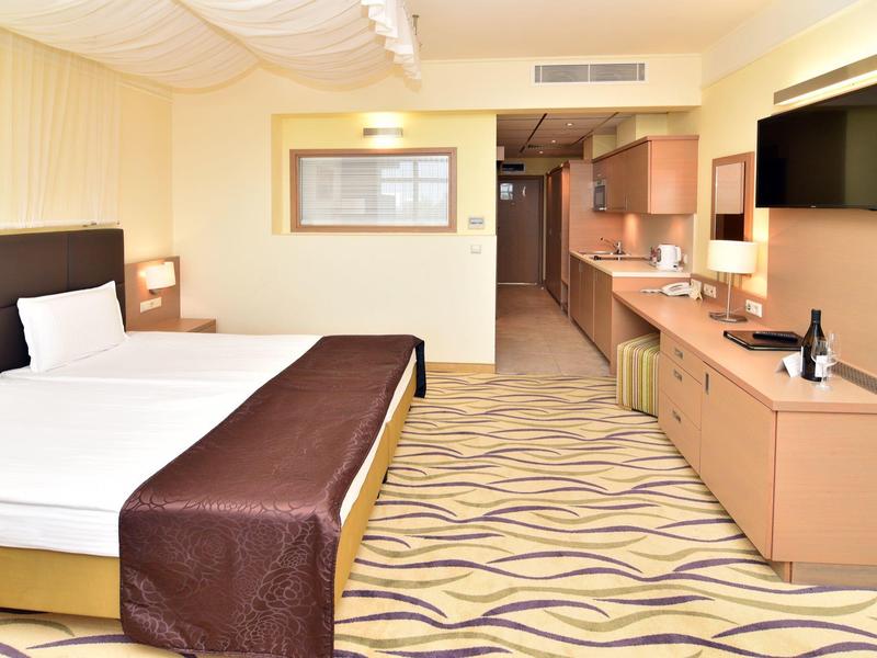 Moderní hotelový pokoj s manželskou postelí, televizí s plochou obrazovkou a dlouhou komodou s minibarem.