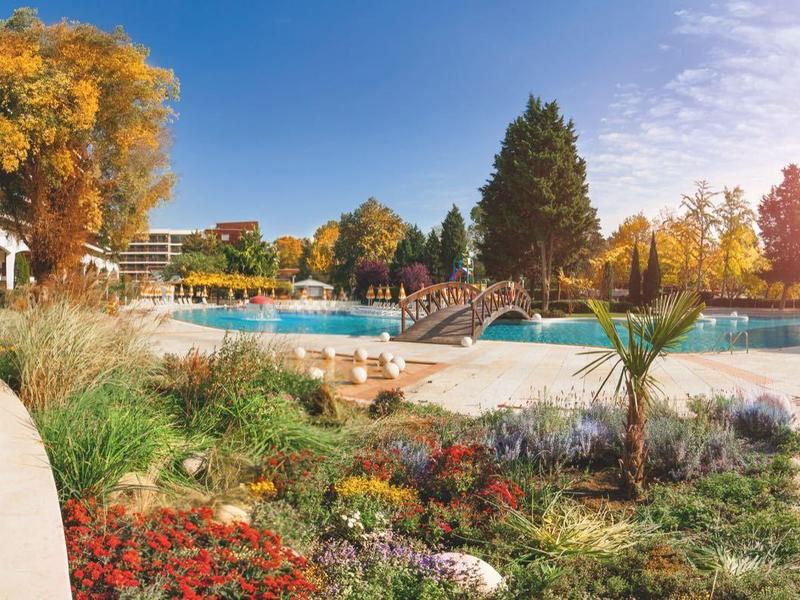 Hotel s bazénem, sluneční terasou a zahradou na podzimní krajině pod jasnou oblohou.